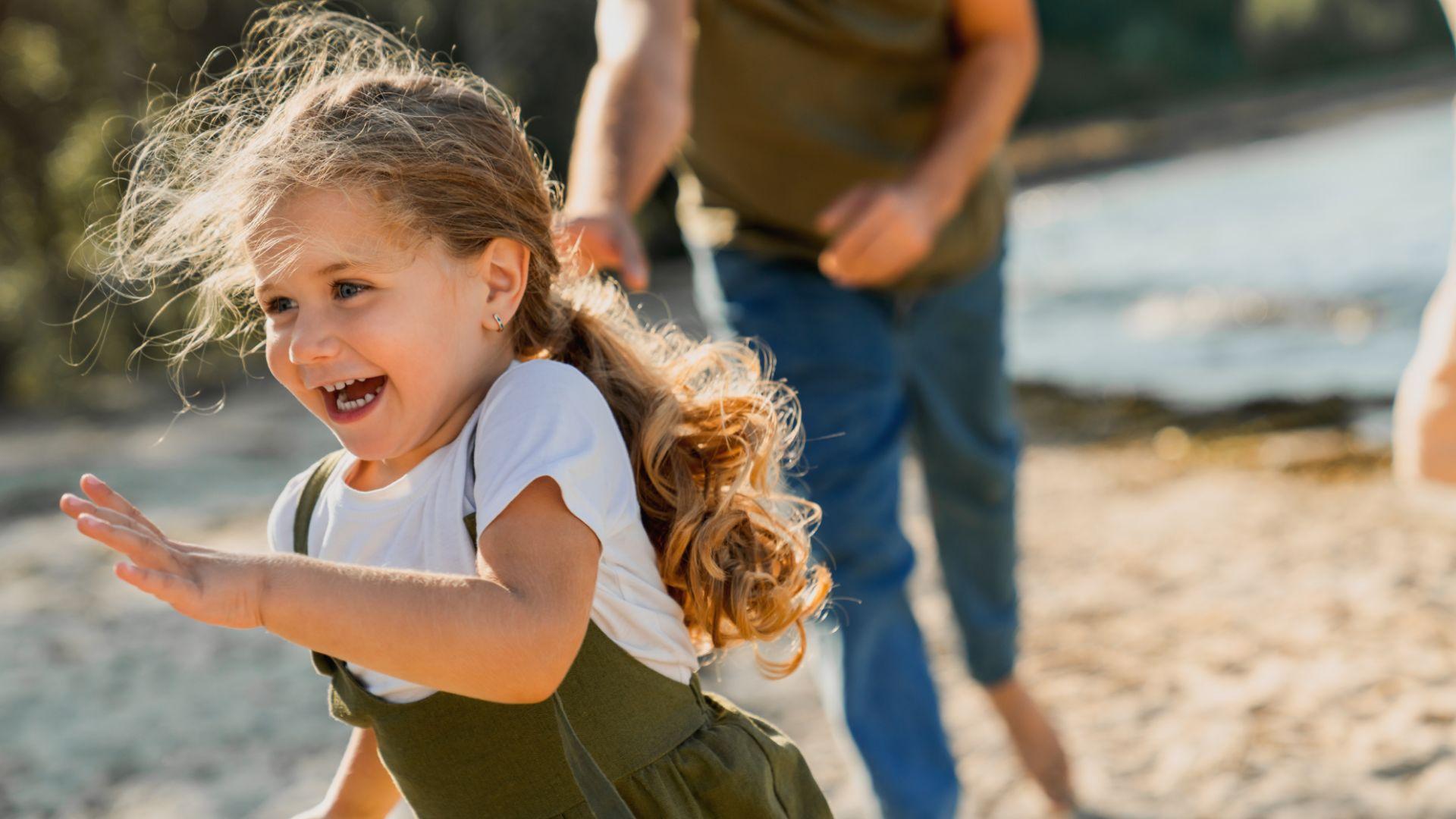 Bambina felice corre sulla spiaggia, seguita da un adulto in una giornata di sole.