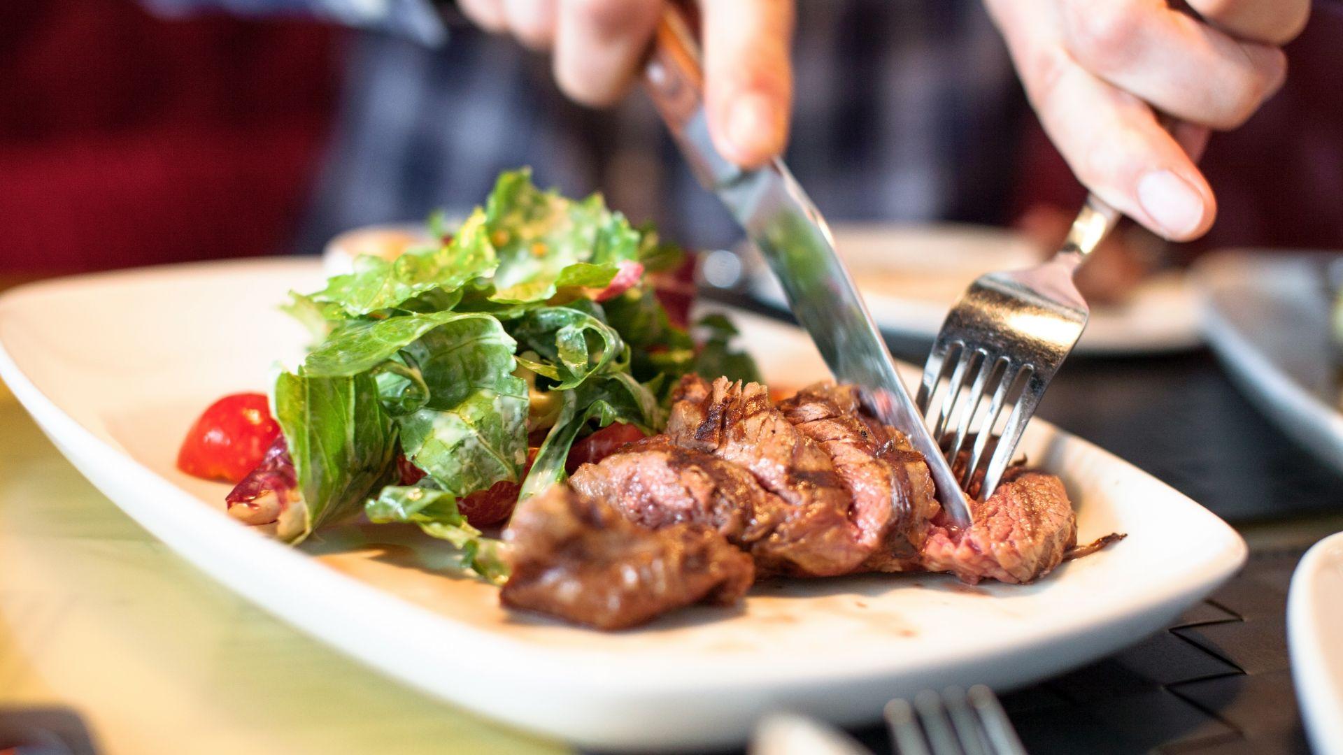 Un piatto di carne con insalata, tagliato con coltello e forchetta.