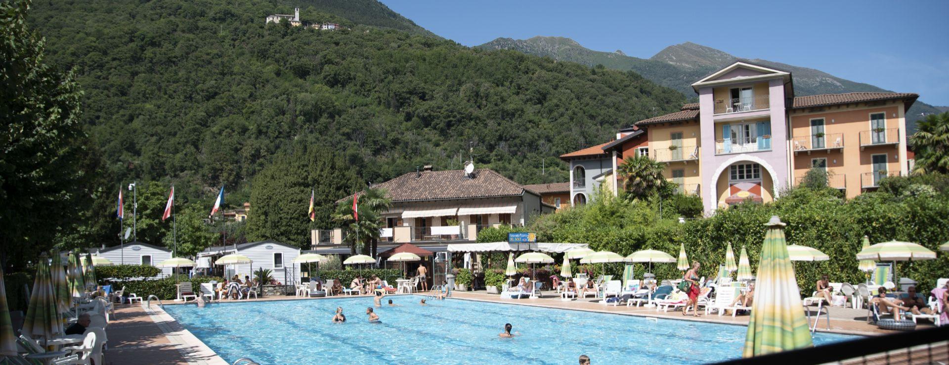 Piscina all'aperto con vista sulle montagne e hotel sullo sfondo.