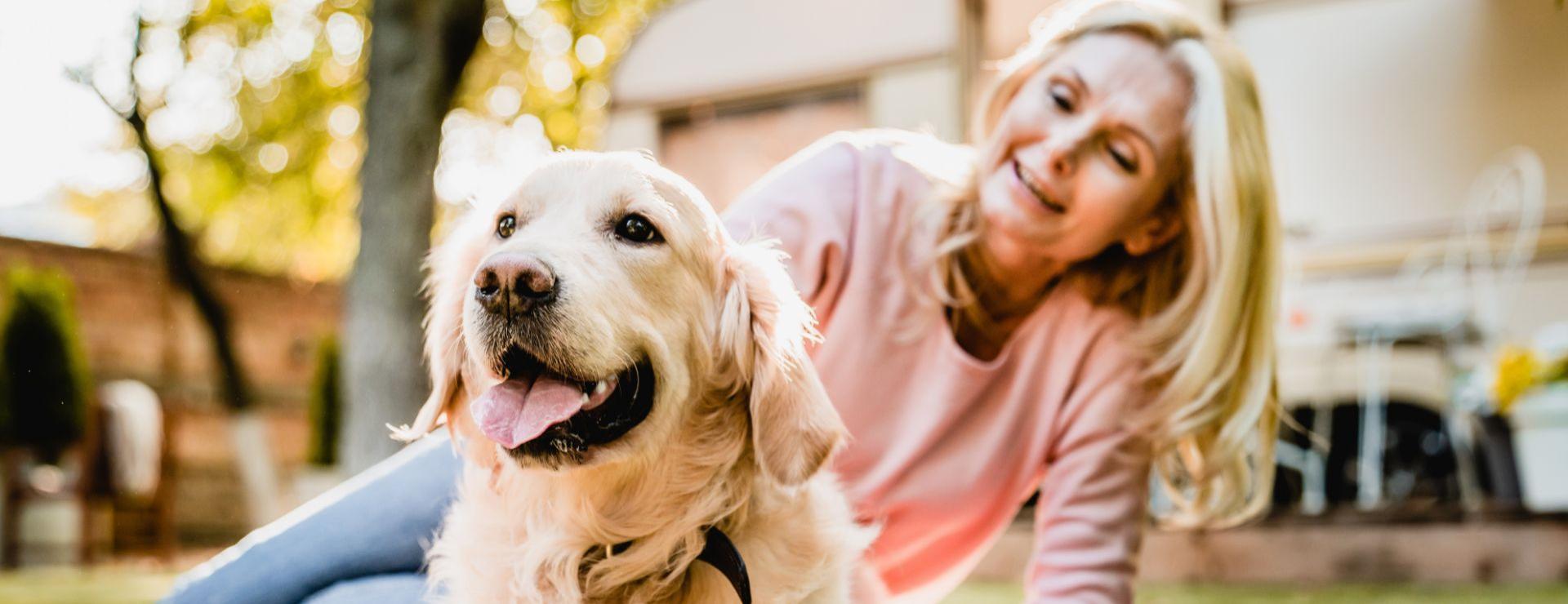 Donna sorridente accarezza un cane all'aperto in una giornata di sole.