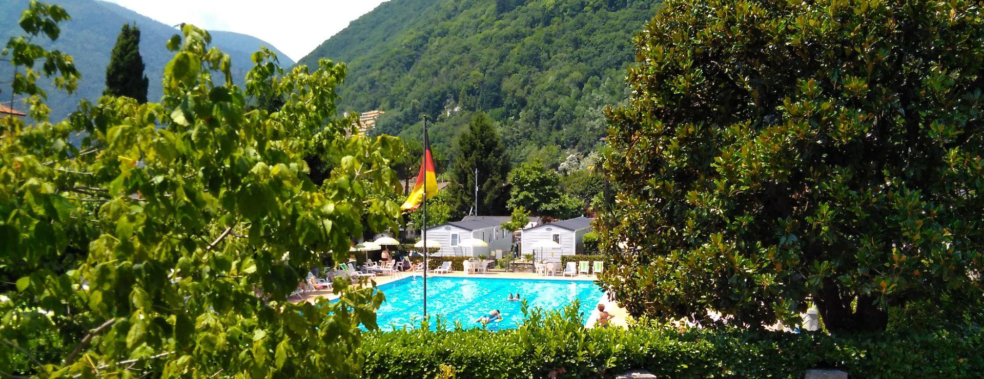 Piscina all'aperto circondata da verde e colline, con bandiera visibile.