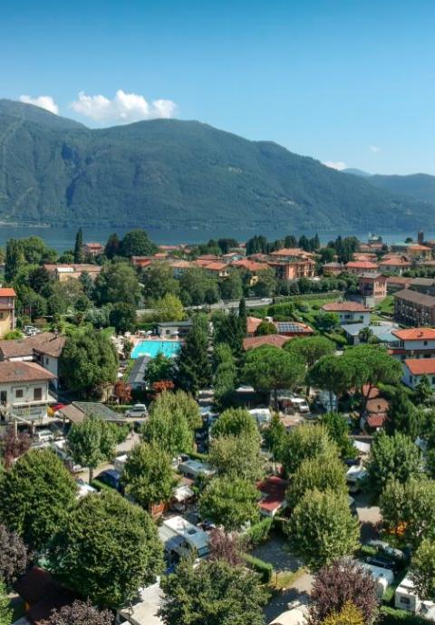 Panorama di un paese con lago, montagne e case immerse nel verde.