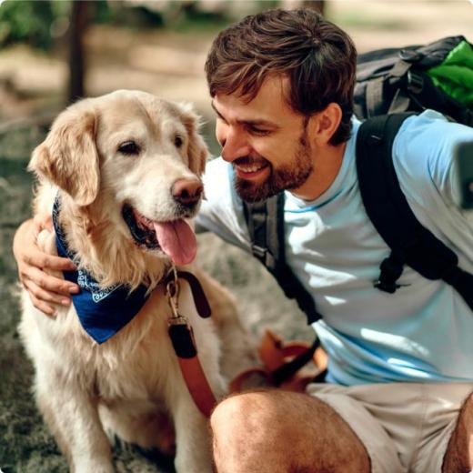 Uomo sorridente accarezza un cane con bandana blu durante un'escursione.