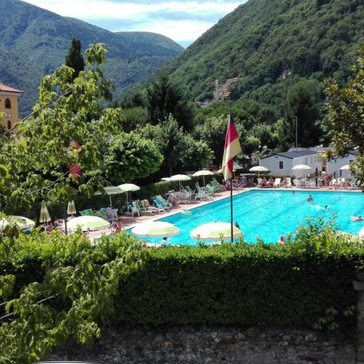 Piscina all'aperto circondata da montagne verdi e ombrelloni colorati.