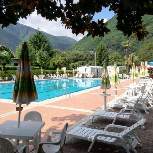 Piscina all'aperto con lettini e ombrelloni, circondata da montagne verdi.