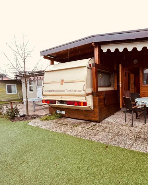 Roulotte con veranda, tavolo esterno e piante, in un'area verde e accogliente.