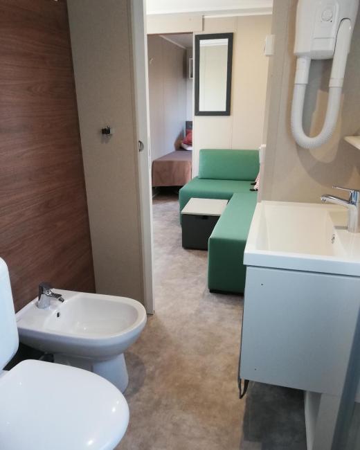 Bagno moderno con bidet, salotto verde e camera da letto sullo sfondo.