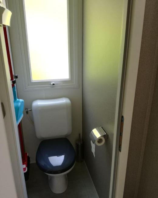 Piccolo bagno con wc, finestra, porta scorrevole e porta carta igienica.