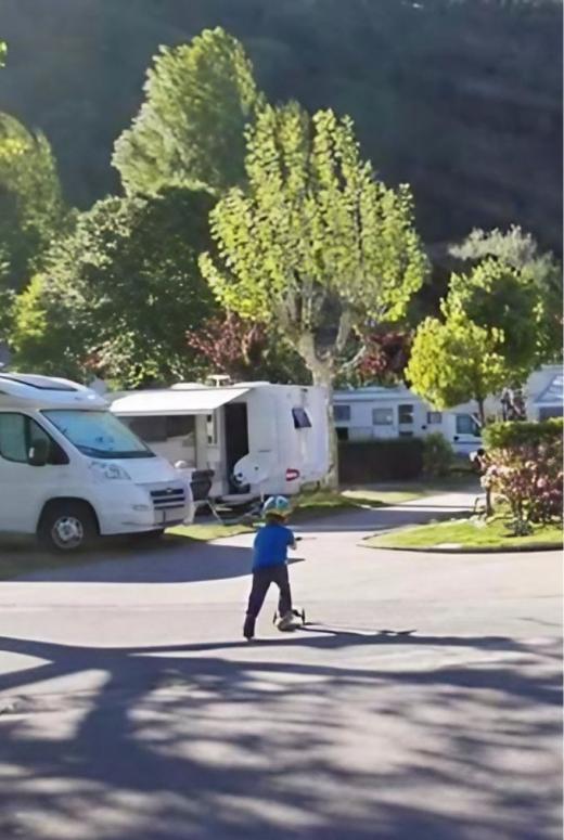 Bambino in monopattino in un campeggio con camper e alberi sullo sfondo.