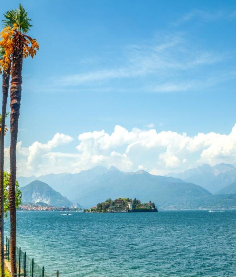 Lago con palme, isola verde e montagne sullo sfondo sotto un cielo azzurro.