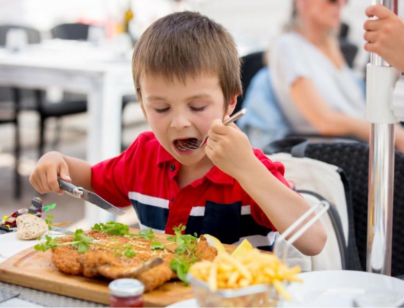 Bambino mangia una cotoletta con patatine in un ristorante all'aperto.