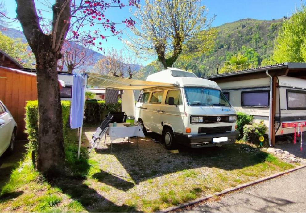 Camper parcheggiato in un'area verde, con tenda aperta e tavolo all'aperto.