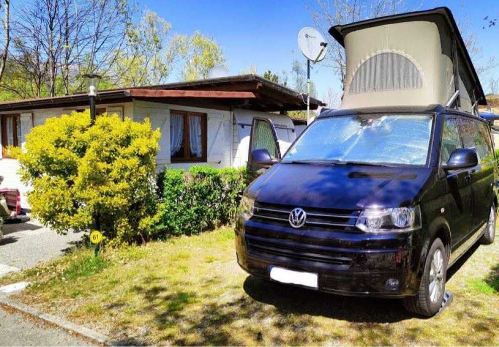 Camper Volkswagen con tetto sollevato parcheggiato vicino a una casa in un campeggio.