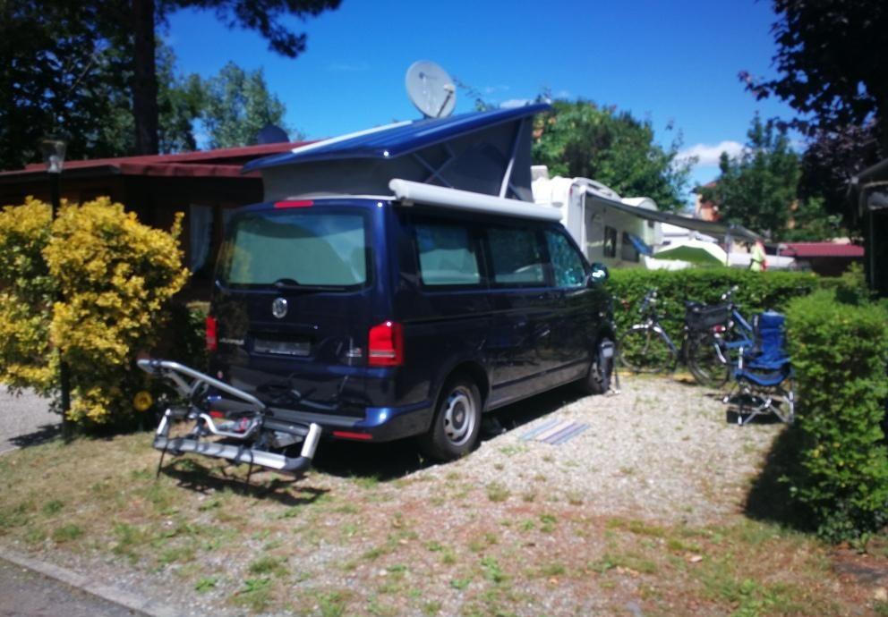 Camper parcheggiato con biciclette e sedie da campeggio in un'area verde.