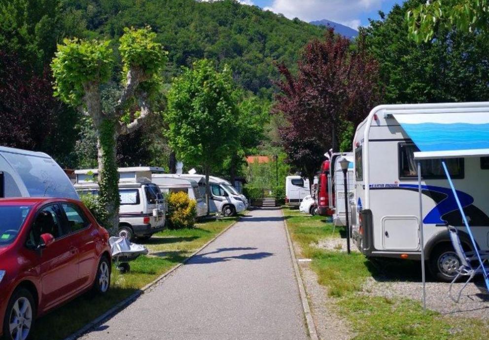 Campeggio con camper e auto, circondato da alberi e colline verdi.