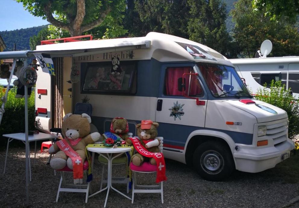 Camper decorato con orsetti e bandiere svizzere, immerso nel verde.