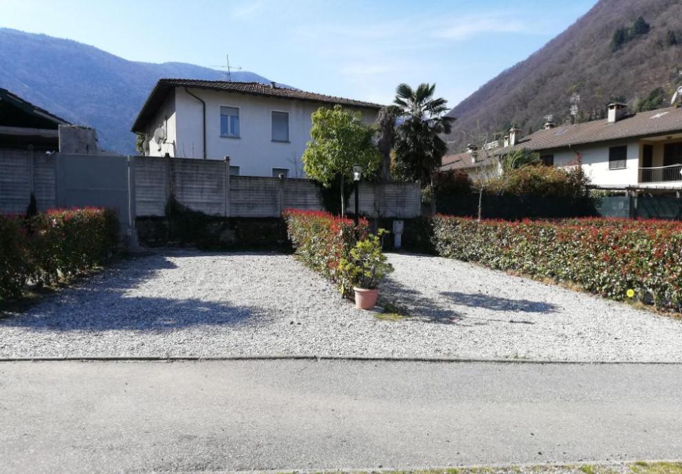 Parcheggio ghiaioso con siepi e montagna sullo sfondo.